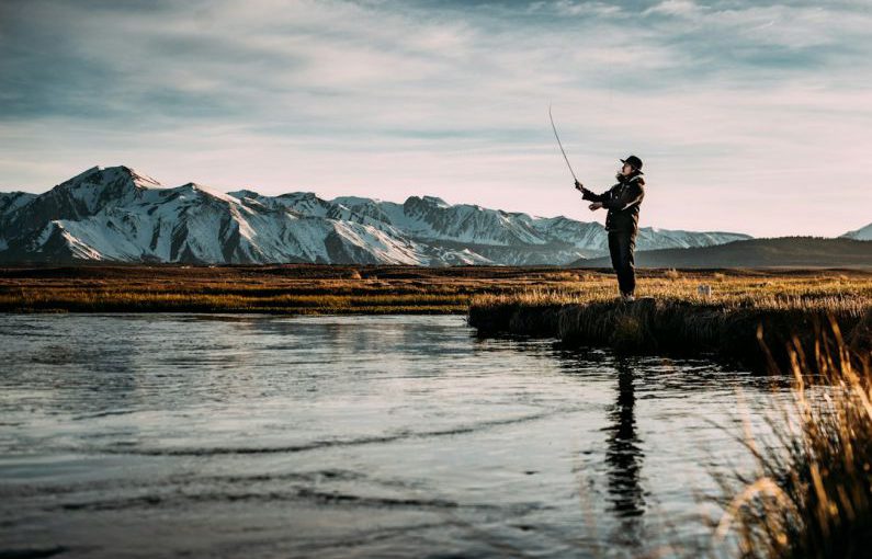 Fly Fishing - landscape photo of man fishing on river near mountain alps