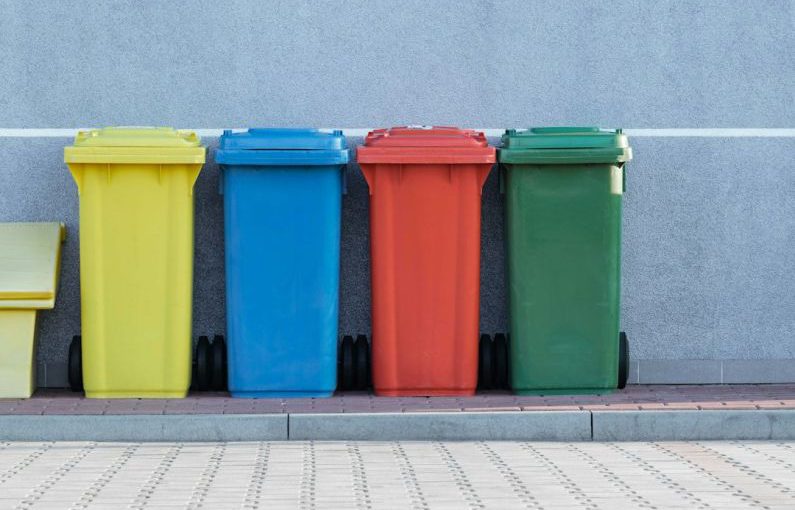 Recycling - four assorted-color trash bins beside gray wall