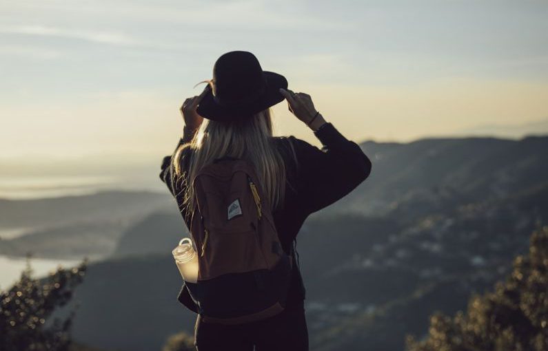 Solo Travel - woman in gray hoodie and black pants wearing black hat standing on top of mountain during