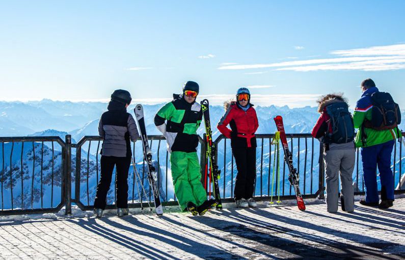 Ski Gear - people in green jacket and blue pants standing on ice field during daytime