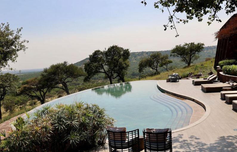 Luxury Lodge - a pool with a patio and chairs