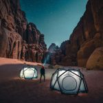 Camping - a man standing next to a tent in the desert
