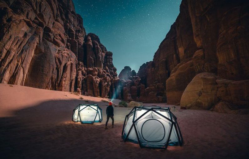 Camping - a man standing next to a tent in the desert