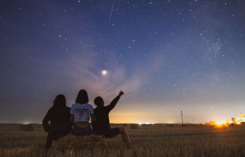 Star Gazing - three person sitting on grass during golden hour