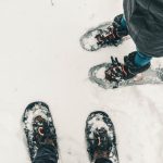 Snowshoeing - person in black pants and black and white snow ski shoes standing on snow covered ground